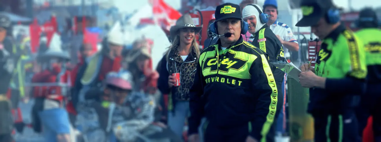 Pit crew chief in a black and yellow City Chevrolet race suit and headset on pit road, from Days of Thunder