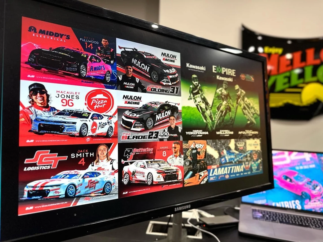 Motorsport autograph cards on a Samsung monitor: a grid of driver cards for Supercars and speedway racers with sponsors including Middy's Electrical, Nulon Racing, Pizza Hut and JCT Logistics, plus a Kawasaki motocross team card